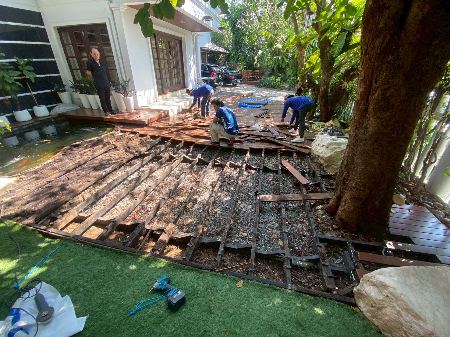 ทีมช่างรื้อแผ่นพื้นไม้เก่าข้างบ้านบริเวณบ่อปลาและต้นไม้